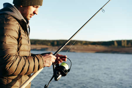 Young fisherman standing on the shore of lake with fishing rodの写真素材