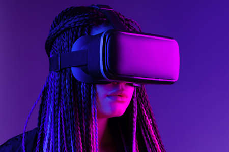 Young woman with afro braids using VR glasses on dark purple neon background