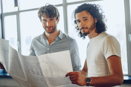 Two young businessmen looking at blueprint and discussing it