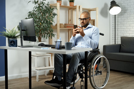 Mixed raced disabled man sitting in a wheelchair and using smartphone