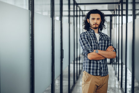 Portrait of young curly casually dressed male entrepreneur standing in a glass corridorの写真素材