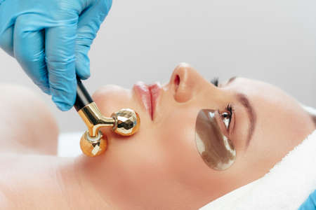 Beautiful woman having face massage with ball roller by cosmetologist