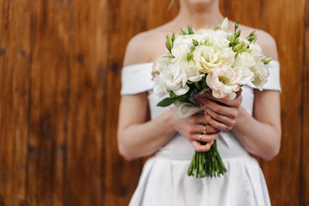 Unrecignizable bride in white dress holding bouquet close up