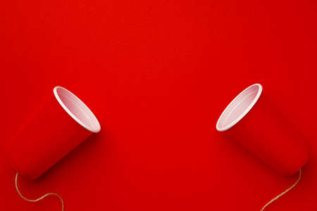Red plastic cups connected with a thread on red backgroundの写真素材