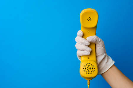 Female hand in medical glove holding yellow telephone speakerの写真素材