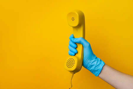 Female hand in medical glove holding yellow telephone speakerの写真素材