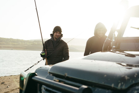 Young fisherman standing near his car and holding fishing equipmentの写真素材