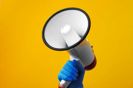 Human hand holding electronic loudspeaker against yellow backgroundの写真素材