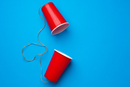 Two red paper cups connected with rope on blue background, toy telephoneの写真素材