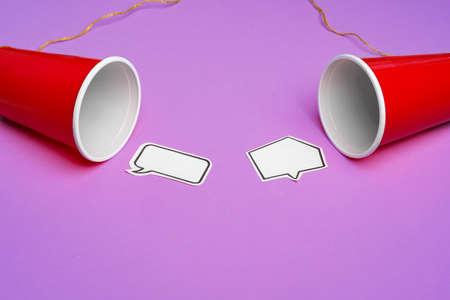 Toy telephone made of plastic cups and string with speech bubbles on purple backgroundの写真素材