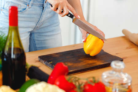 Woman cuts yellow bell pepper for salad on wooden tableの写真素材