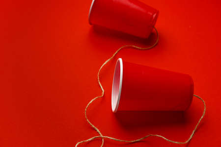 Red plastic cups connected with a thread on red backgroundの写真素材