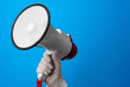 Hand in medical glove holding loudspeaker against blue backgroundの写真素材