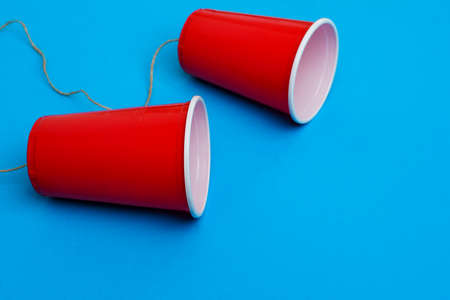 Two red paper cups connected with rope on blue background, toy telephoneの写真素材