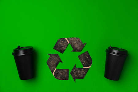 Disposable coffee cup and recycling sign on green backgroundの写真素材