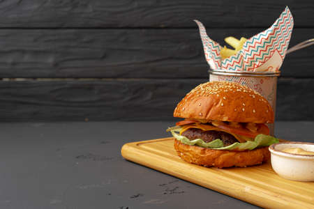 Delicious burger and fries on wooden board against black backgroundの写真素材