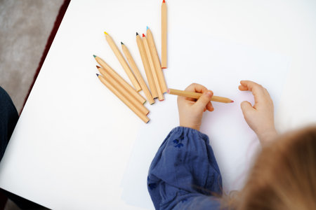Little girl drawing on big white sheet of paper top view