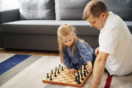 Grandfather and granddaughter playing chess together at homeの写真素材