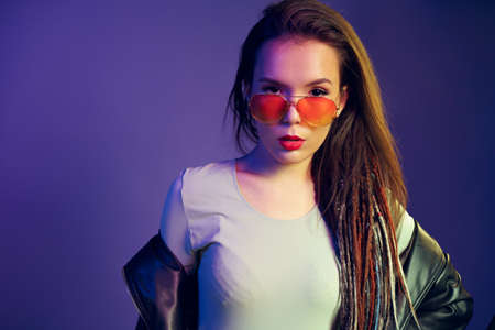 Asian girl in sunglasses and black leather jacket posing against dark blue background