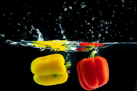 Bell pepper falling into water with a splash against black backgroundの写真素材