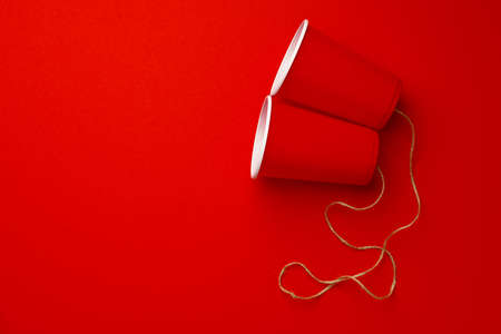 Red plastic cups connected with a thread on red background