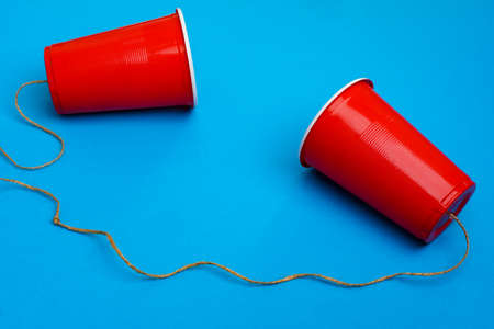Two red paper cups connected with rope on blue background, toy telephoneの写真素材