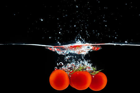 Tomatoes falling into the water with a splash against black backgroundの写真素材