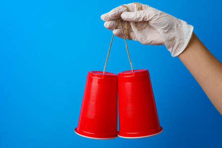 Hand in medical glove holding toy telephone made of plastic cup and string