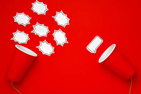 Toy telephone made of plastic cup and string on red background with speech bubbleの写真素材