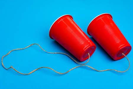 Two red paper cups connected with rope on blue background, toy telephoneの写真素材