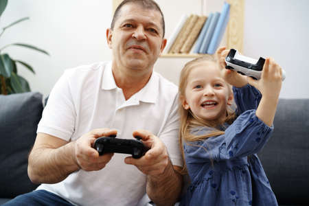 Grandfather and granddaughter playing video games at home.