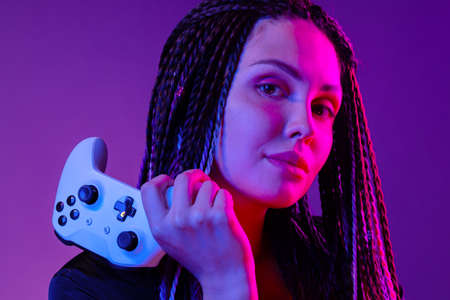 Young woman with long braids holding console joystick against dark purple background