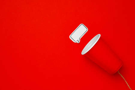 Toy telephone made of plastic cup and string on red background with speech bubbleの写真素材