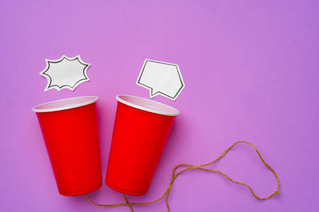 Toy telephone made of plastic cups and string with speech bubbles on purple backgroundの写真素材
