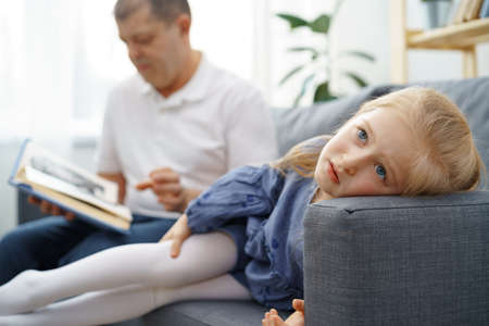 Grandfather reading a book to his little graddaughter in living roomの写真素材