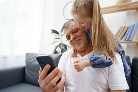 Grandfather and little granddaughter watching something on smartphone at home