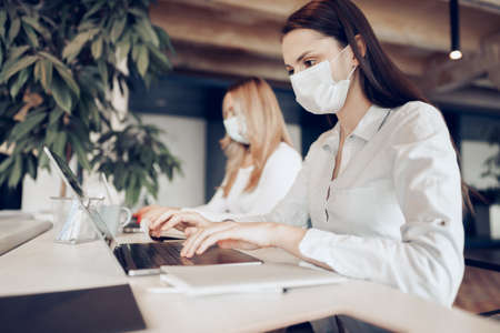 Two female colleagues working in office together wearing medical masksの写真素材