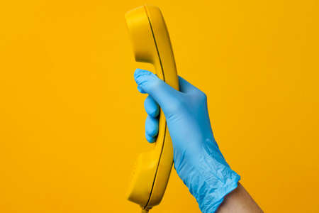 Female hand in medical glove holding yellow telephone speakerの写真素材
