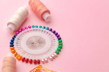 Sewing accessories including thread spools and pins on pink backgroundの写真素材