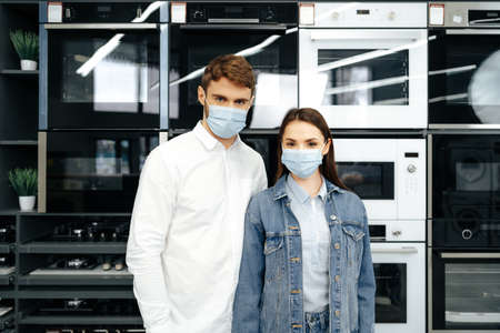 Young couple wearing medical masks in hypermarket with home appliancesの写真素材