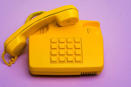 Yellow landline telephone on purple background close up