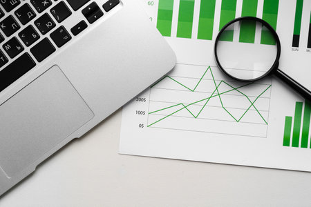 Top view of laptop and printed charts on office tableの写真素材