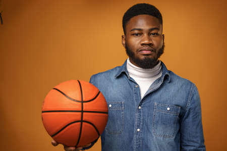 African american man holding basketball ball and looking at camera on yellow background