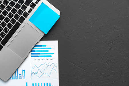 Printed graphs and laptop on dark gray surfaceの写真素材