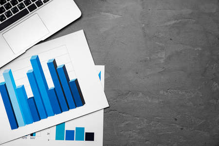 Printed graphs and laptop on dark gray surface