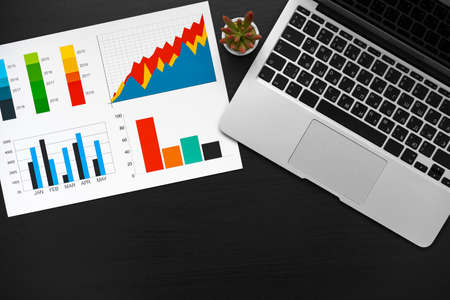 Printed graphs and laptop on dark gray surfaceの写真素材