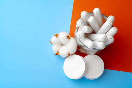 Female medical tampons and cotton flower on blue paper background