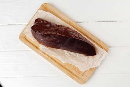 Raw beef liver on wooden board on table