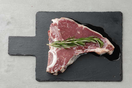 Raw t-bone steak marinated in oil on gray table