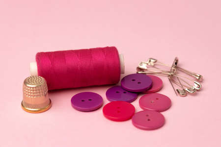 Sewing accessories including thread spools and pins on pink backgroundの写真素材